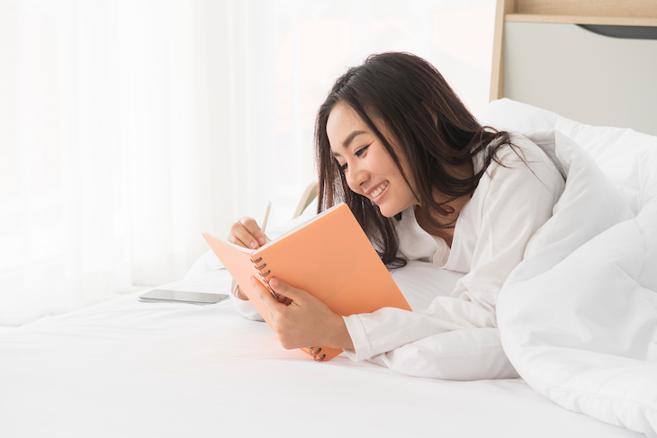 Young woman writing in a journal while lying in bed